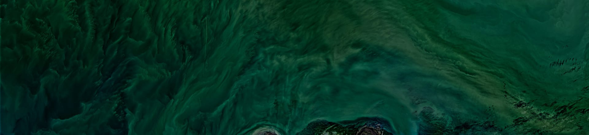 Aerial satellite view of turquoise water currents swirling across a coastal surface.